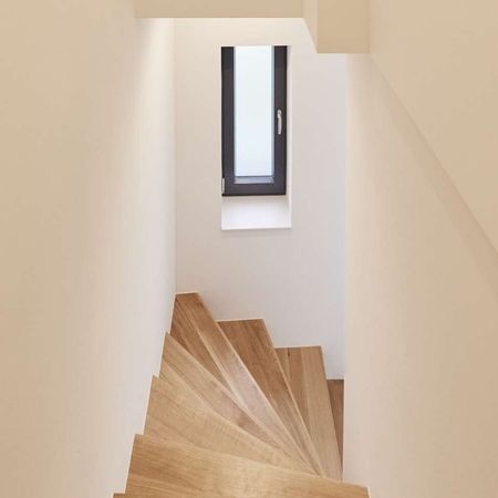 Ein schmaler Flur mit Holztreppe und weißen Schränken an den Wänden.