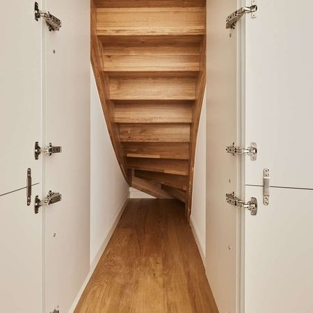 Ein schmaler Gang, der eine Holztreppe und weiße Schränke zeigt.